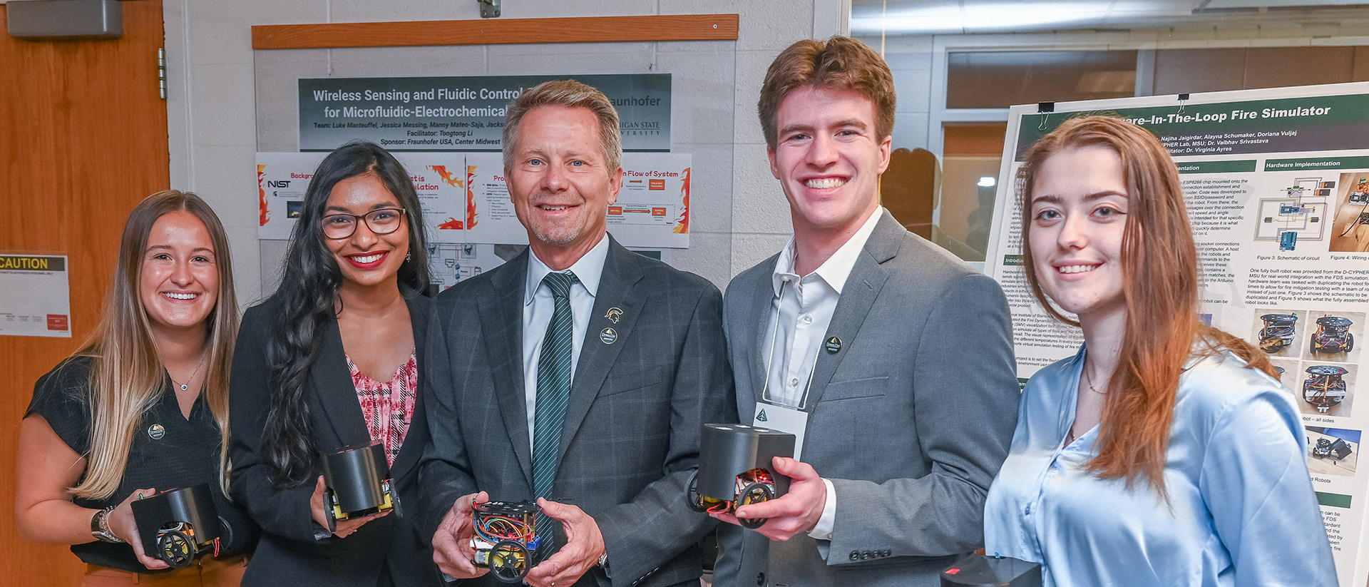 President Guskiewicz posing with students in front of a project poster at Design Day.